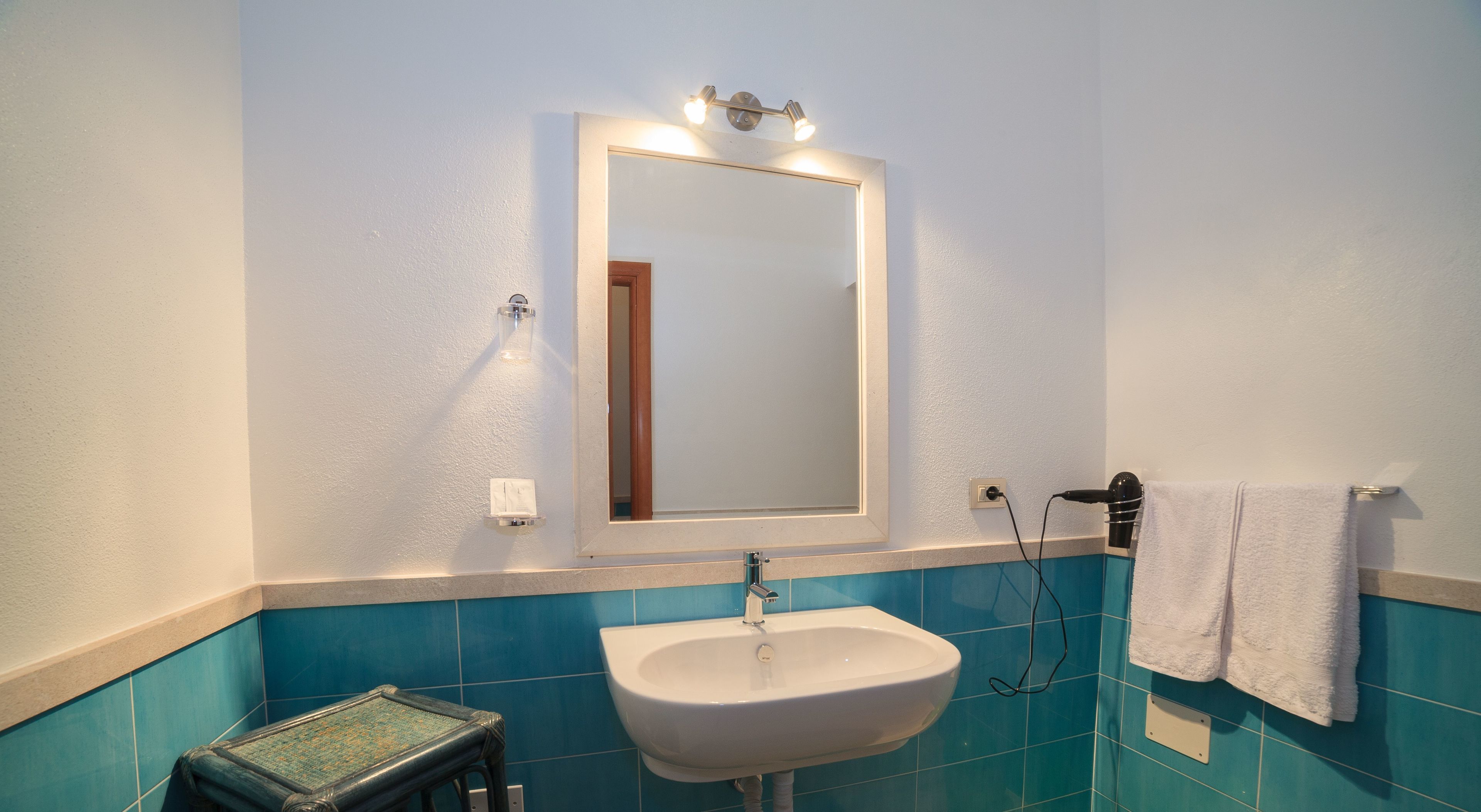 A bathroom with a white sink, a mirror with lights, and blue tiles.
