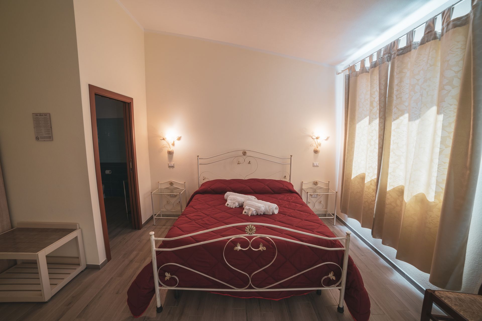A neatly arranged bedroom with a bed, bedside tables, and a window with curtains.