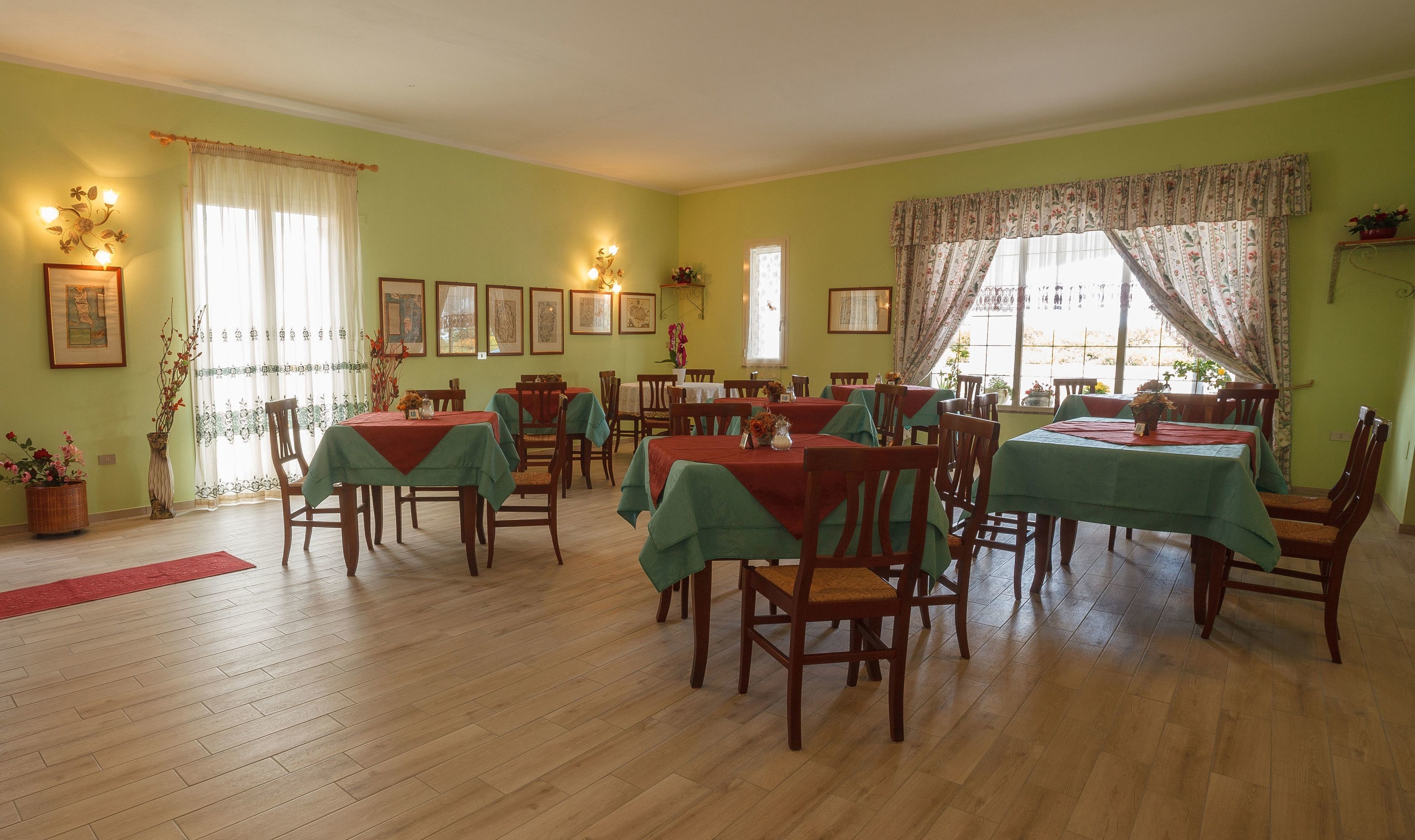 Comedor con varias mesas y sillas, manteles verdes, suelo de madera y adornos florales.