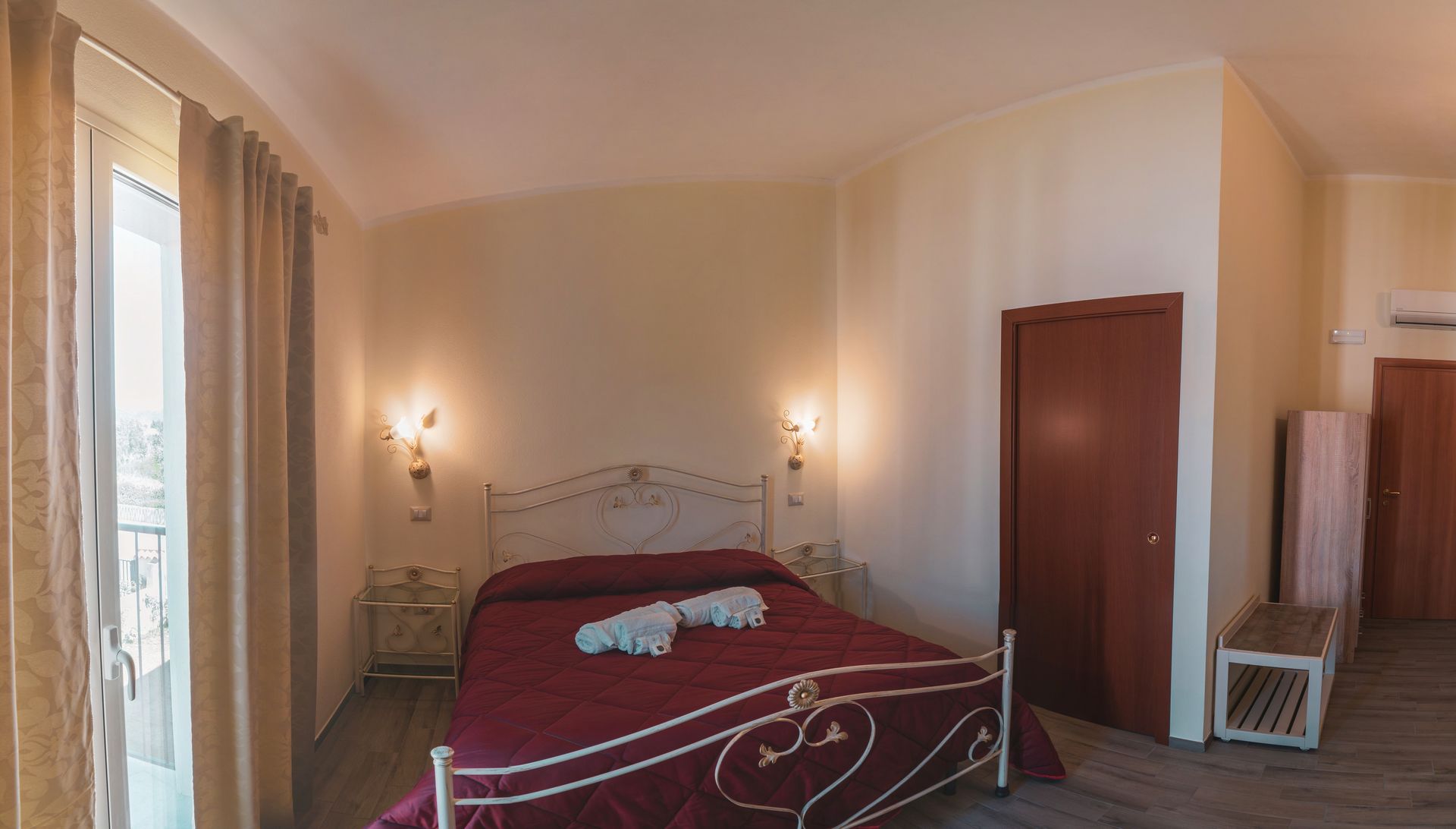 Une chambre à coucher avec un lit, deux lampes fixées au mur, une porte en bois et une petite table.