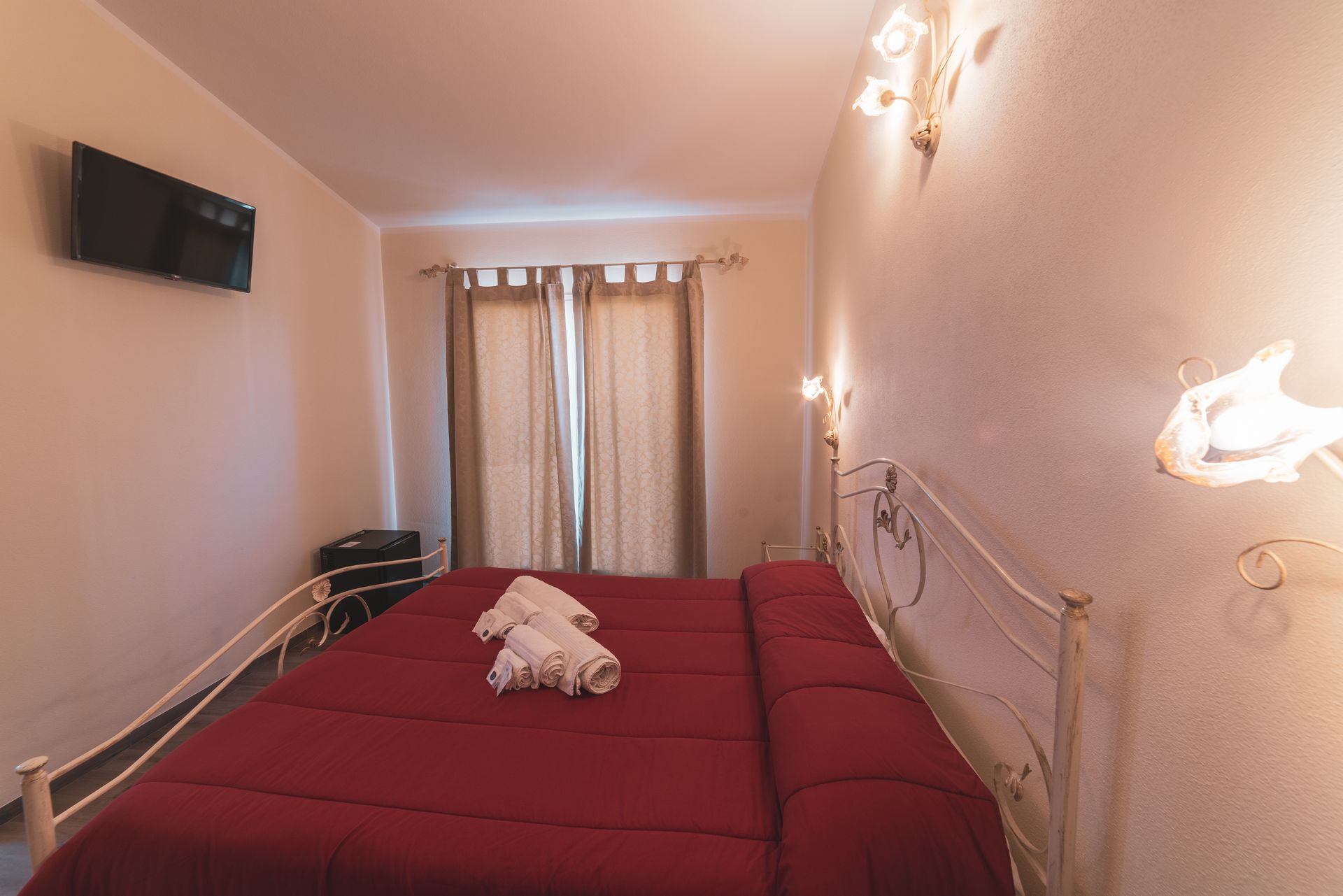 Une chambre d’hôtel avec un lit, des rideaux, une télévision et des lampes fixées au mur.