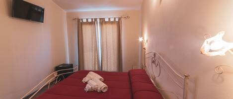 Une chambre d’hôtel avec un lit, des rideaux, une télévision et des lampes fixées au mur.
