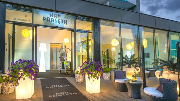 Entrada de hotel con un cartel que dice "NAD PARSETA" y un área de estar al aire libre con macetas.