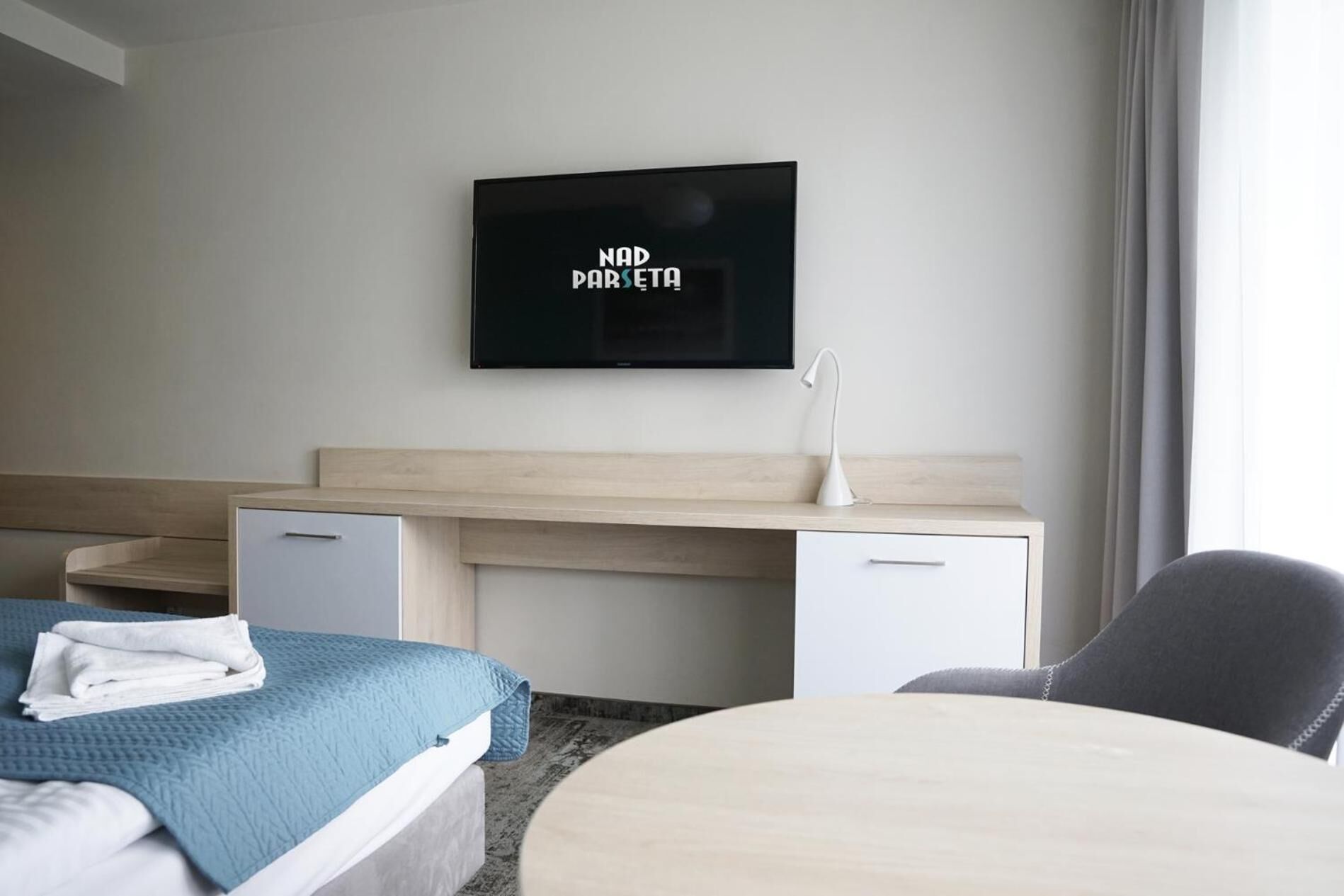 A hotel room with a bed, a desk, a chair, a TV, and a bedside table.