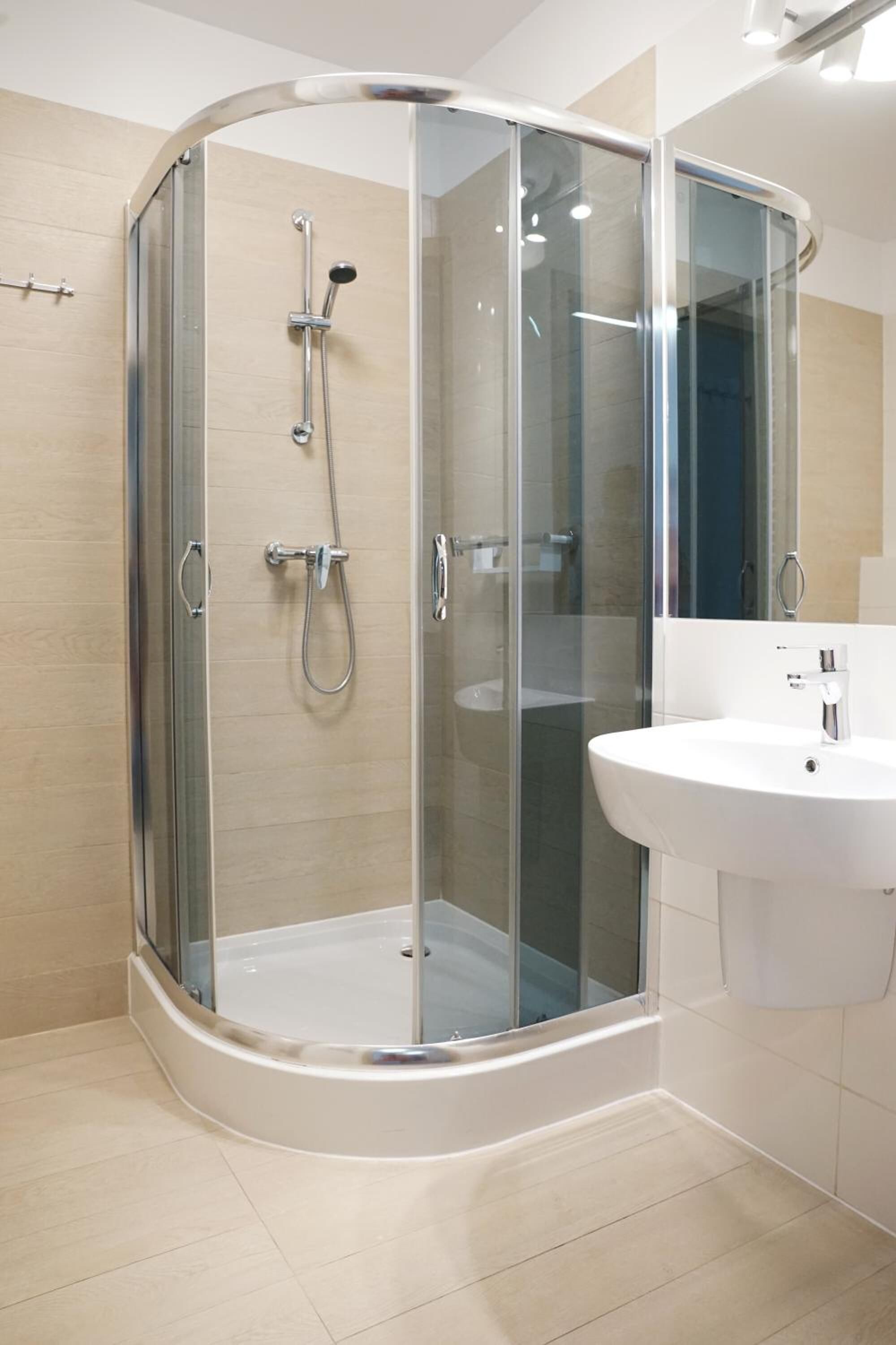Une salle de bain moderne avec une douche à parois de verre, un lavabo blanc et des murs recouverts de carreaux beiges.
