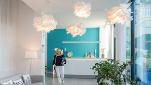 Una zona de recepción moderna con una pared de acento color turquesa, un mostrador de recepción y una planta grande en maceta.