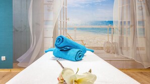 Una habitación con vista a la playa, una mesa de masaje con toallas y una flor.