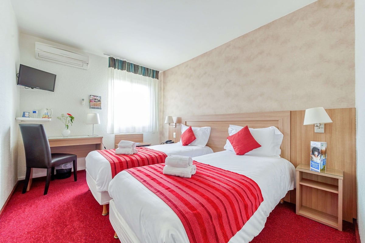 A hotel room with two beds, a desk, a chair, a TV, and a window with curtains.