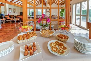 Un bufé de desayuno con diversos pasteles, frutas y cestas de pan.