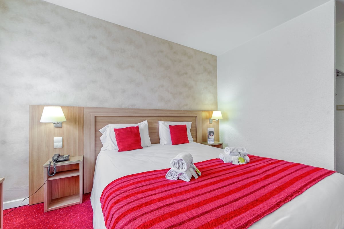 A hotel room with a large bed, red and white bedding, two bedside lamps, a wooden nightstand with a phone, and a red-striped throw blanket.