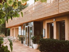 Entrada de hotel con fachada de madera, puertas de cristal y zona de estar al aire libre.