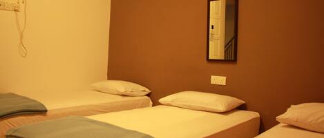 Habitación de hotel con dos camas individuales, cada una con una almohada y una colcha. Un espejo está fijado a la pared sobre una de las camas.