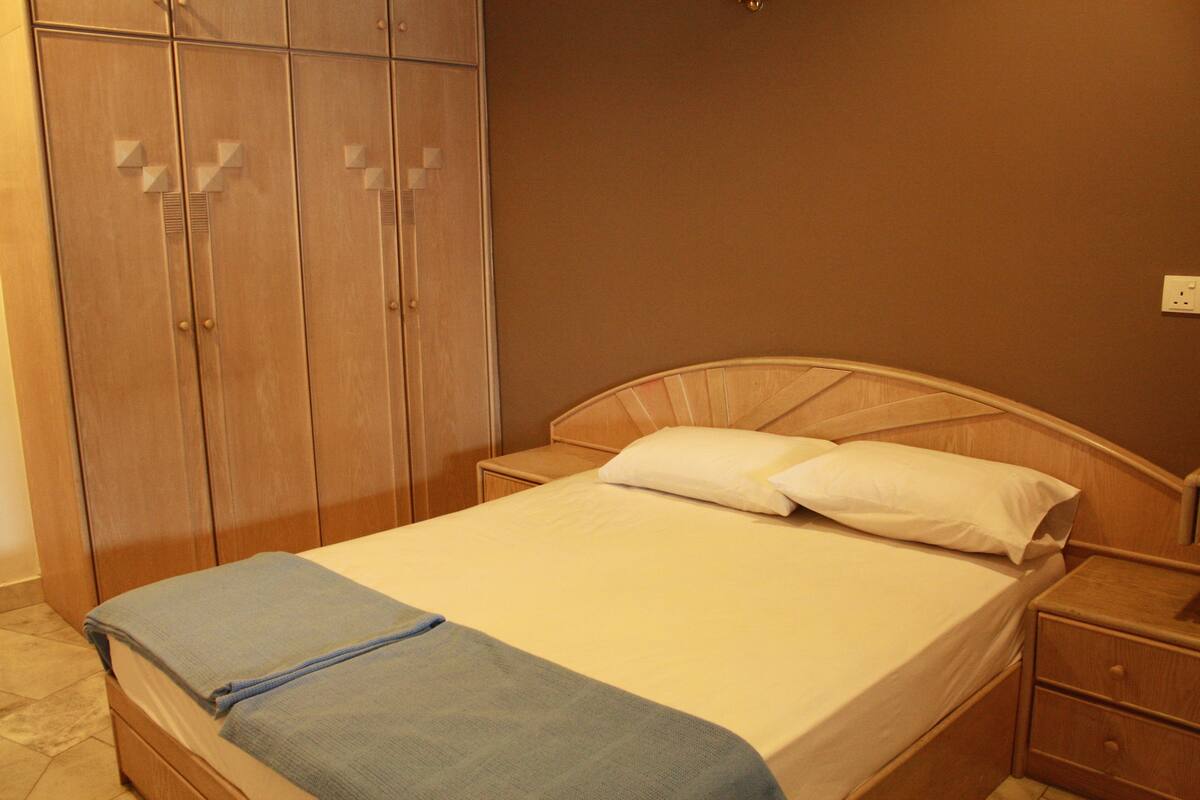 A bedroom with a wooden bed, a nightstand, a wardrobe, and a wall socket.