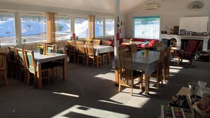 Un comedor acogedor con mesas y sillas de madera, ventanas amplias con vistas nevadas y una chimenea con cuadros enmarcados.