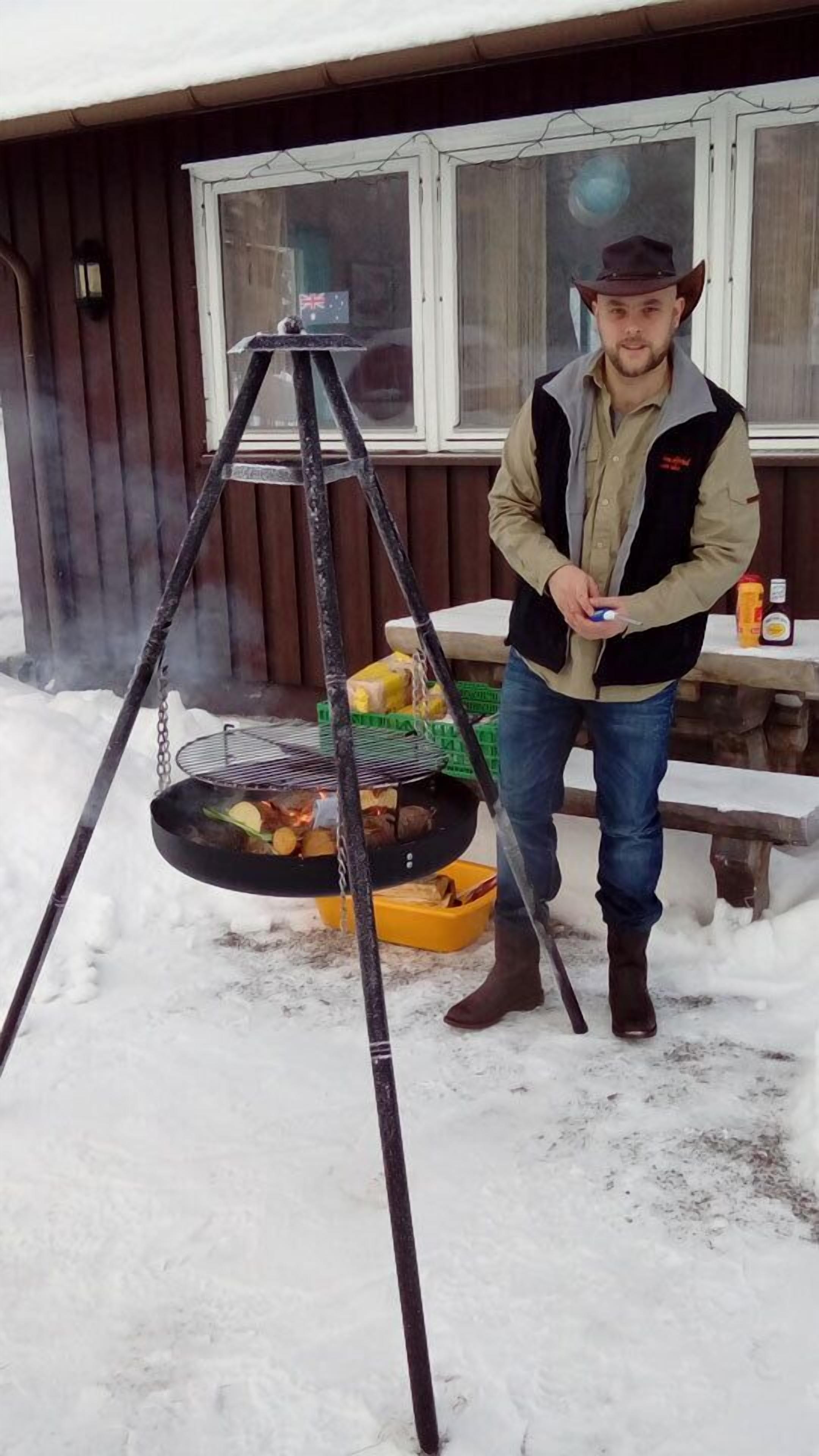 A person standing next to a portable grill outdoors with snow on the ground.