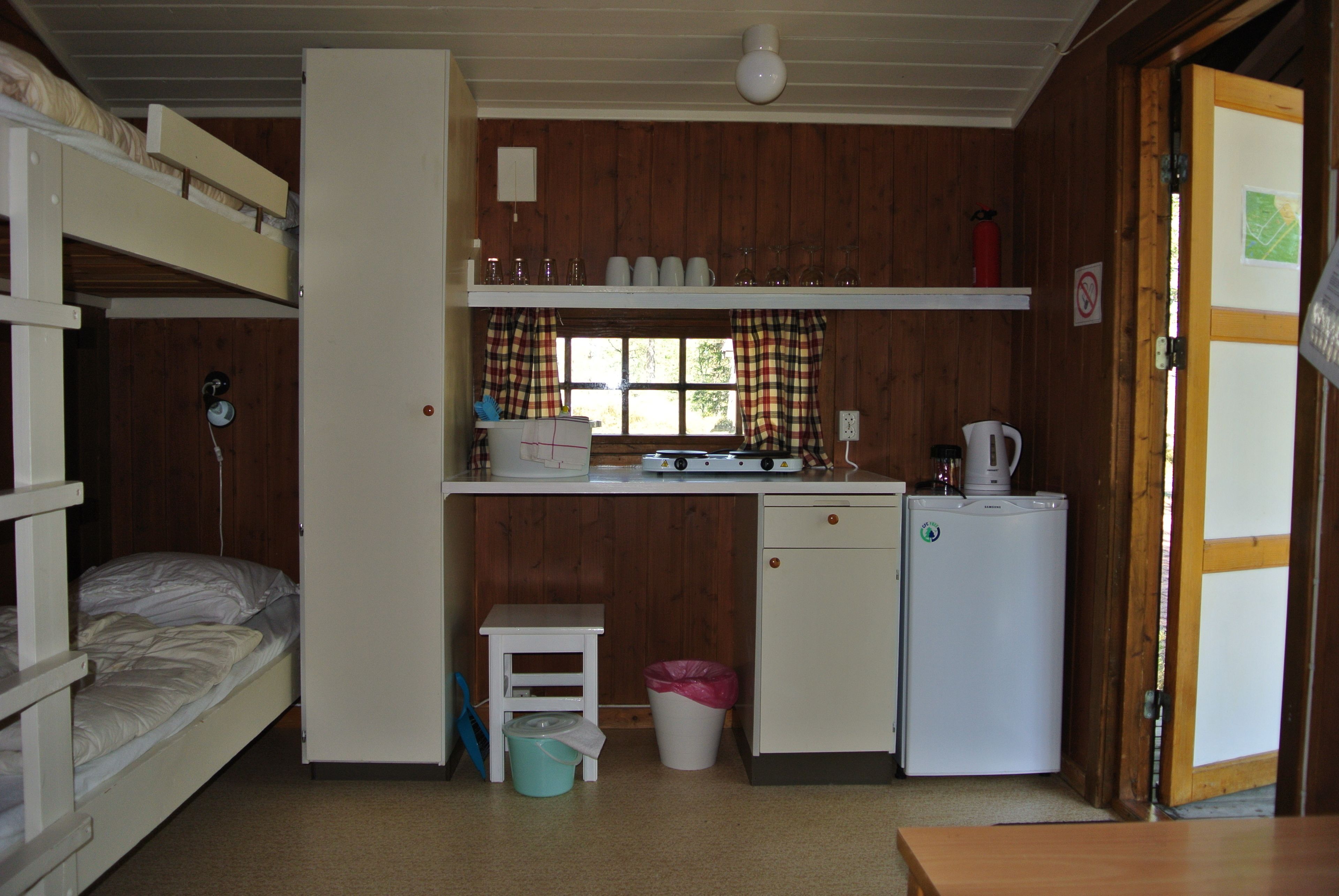 A compact cabin with bunk beds, a kitchenette, a small table, and a window with curtains.
