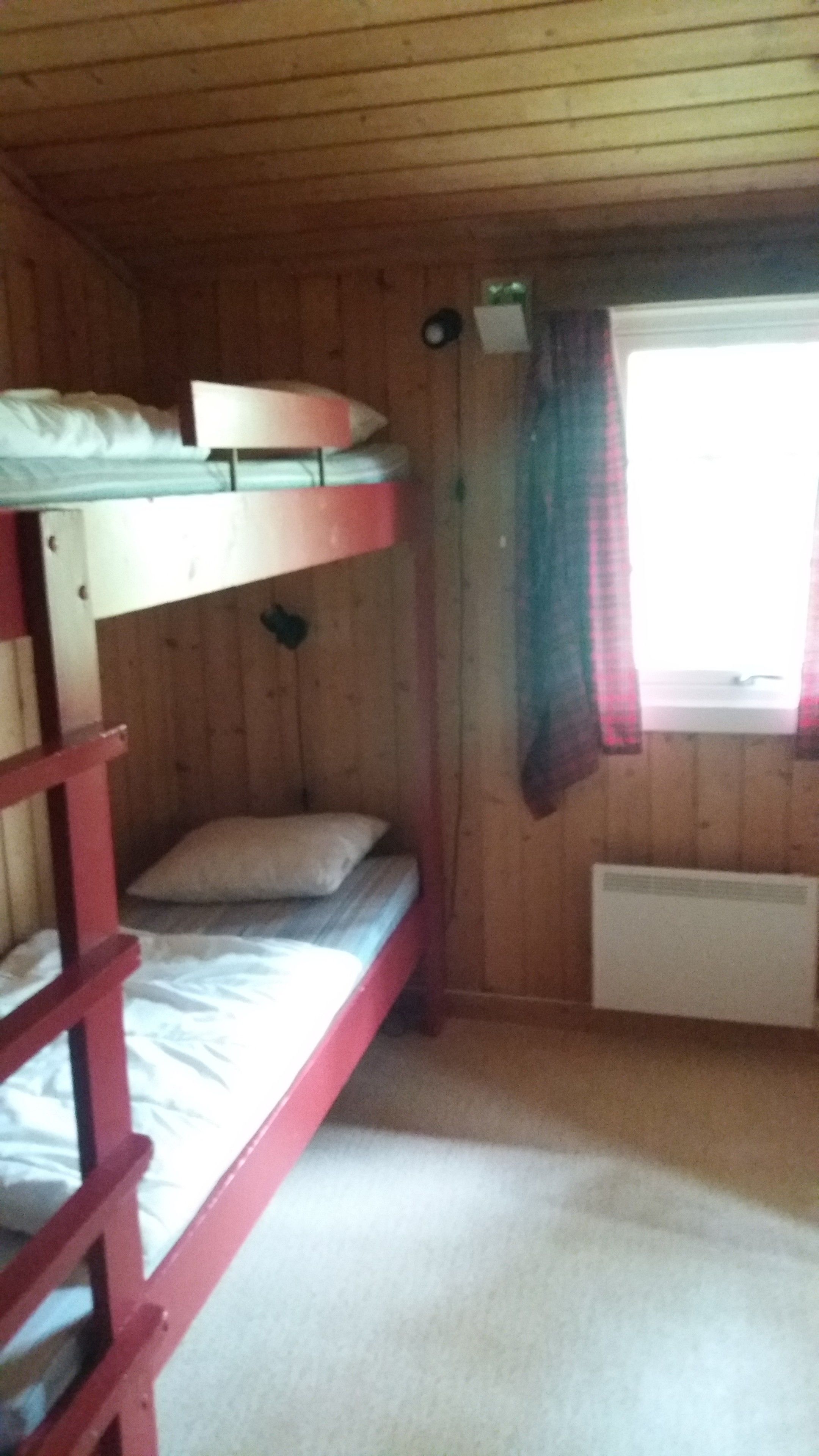 A bunk bed room with a wooden ceiling, a window with curtains, and a radiator.