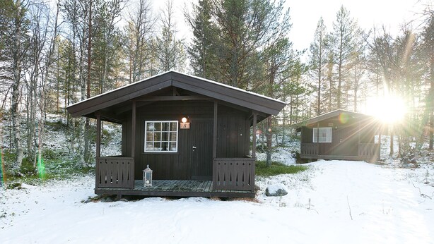 Una cabaña con porche y puerta, rodeada de nieve y árboles.
