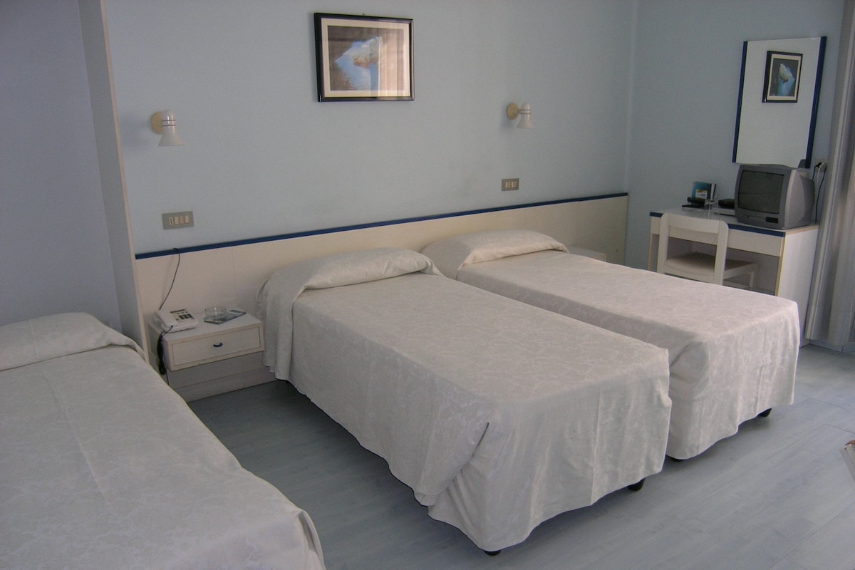A hotel room with two single beds, a desk with a computer, and a small table.