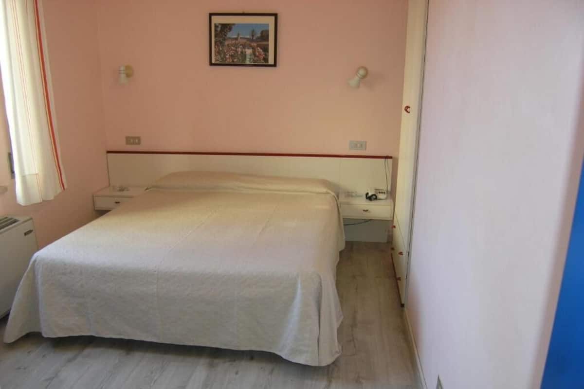 A bedroom with a bed, bedside tables, a nightstand, a wall-mounted light, and a painting.