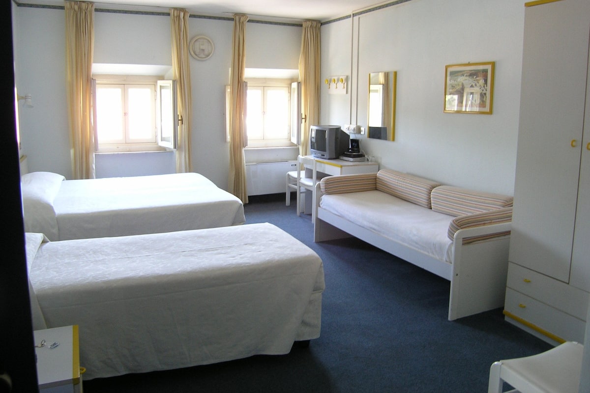 A hotel room with two single beds, a sofa, a desk with a computer, and a wardrobe.