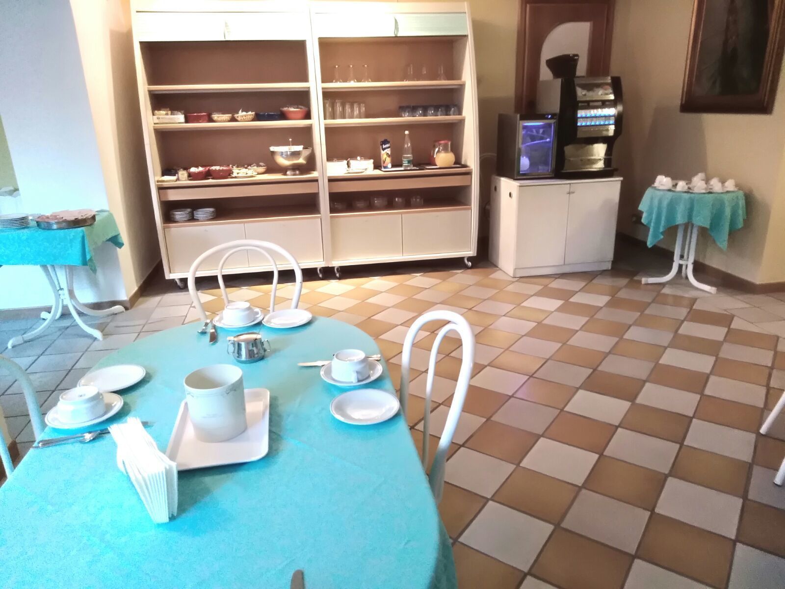 A dining area with a blue table set for four, white chairs, and a buffet counter with shelves of dishes and glasses.