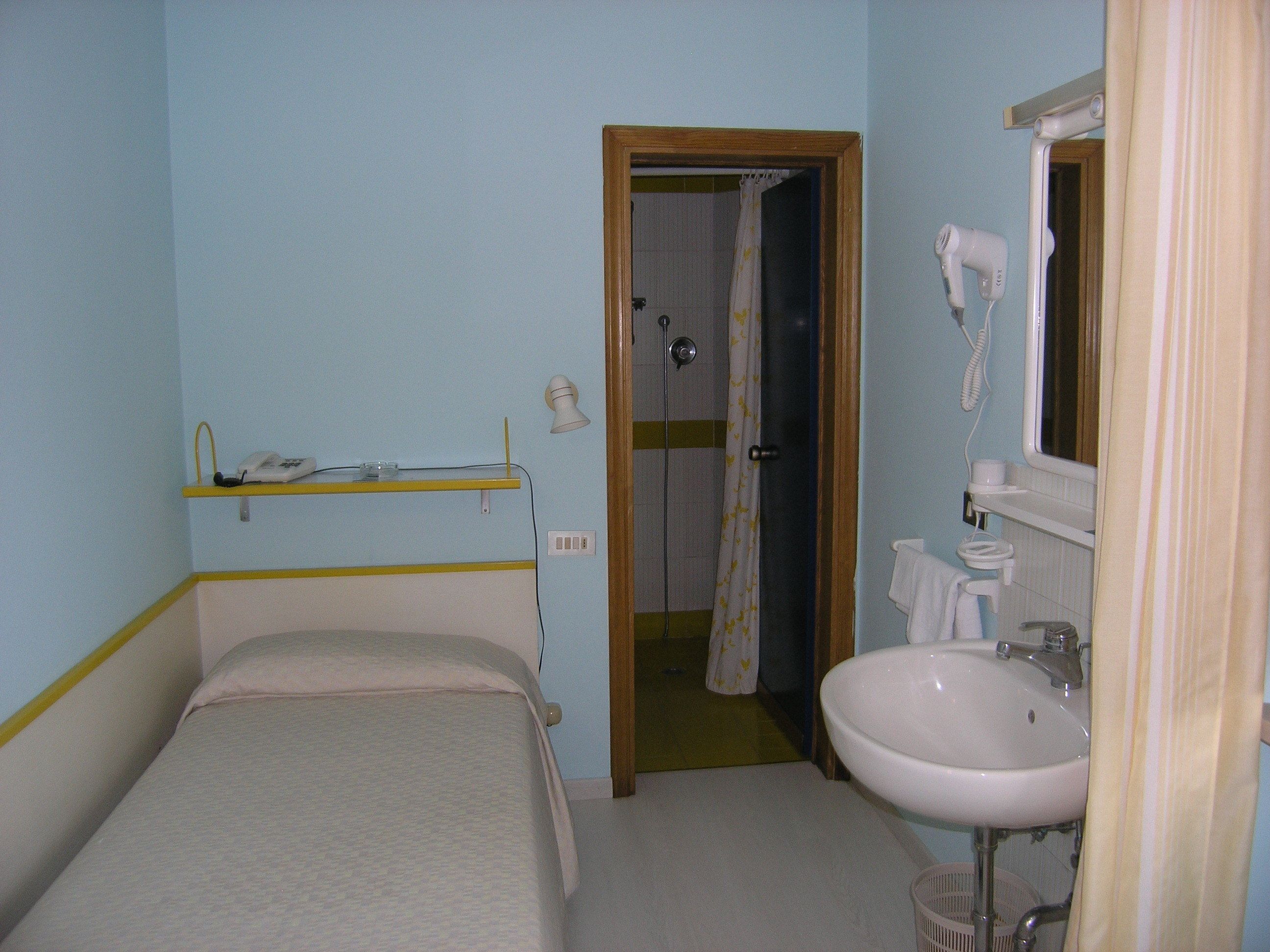 A small, single-bed room with a bathroom containing a sink, mirror, and hairdryer.