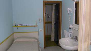 A small, single-bed room with a bathroom containing a sink, mirror, and hairdryer.