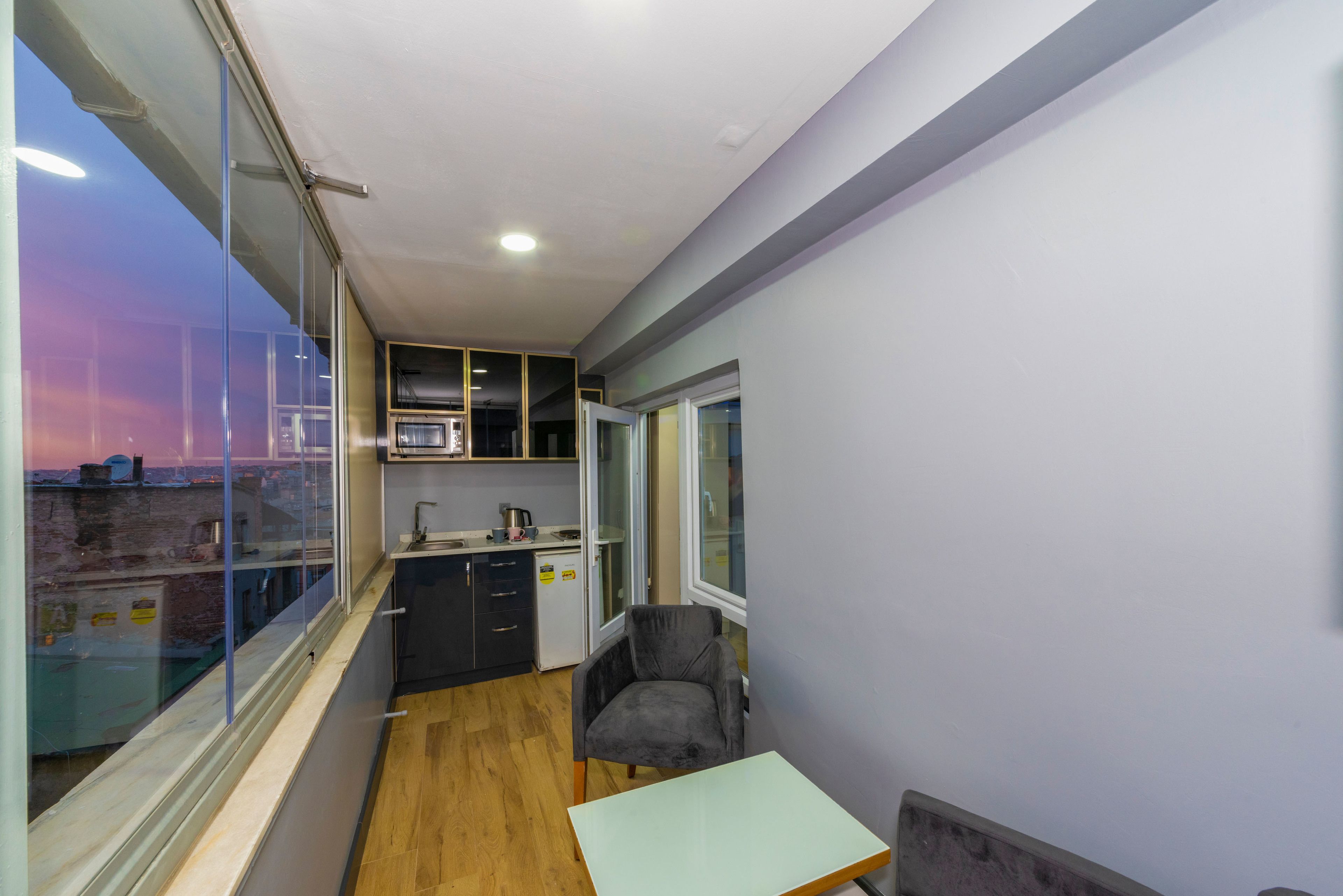 A compact kitchen with a microwave, sink, and cabinets, a small table, and a chair.