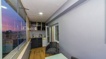 A compact kitchen with a microwave, sink, and cabinets, a small table, and a chair.