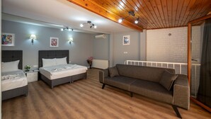 A bedroom with two beds, a gray sofa, wooden ceiling, and a white brick wall. - Butterfly Suites (Istanbul)