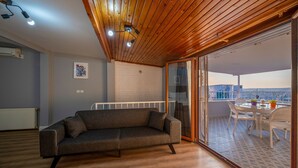 A modern living room with a wooden ceiling, a grey sofa, and a glass door leading to an outdoor dining area with white furniture. - Butterfly Suites (Istanbul)
