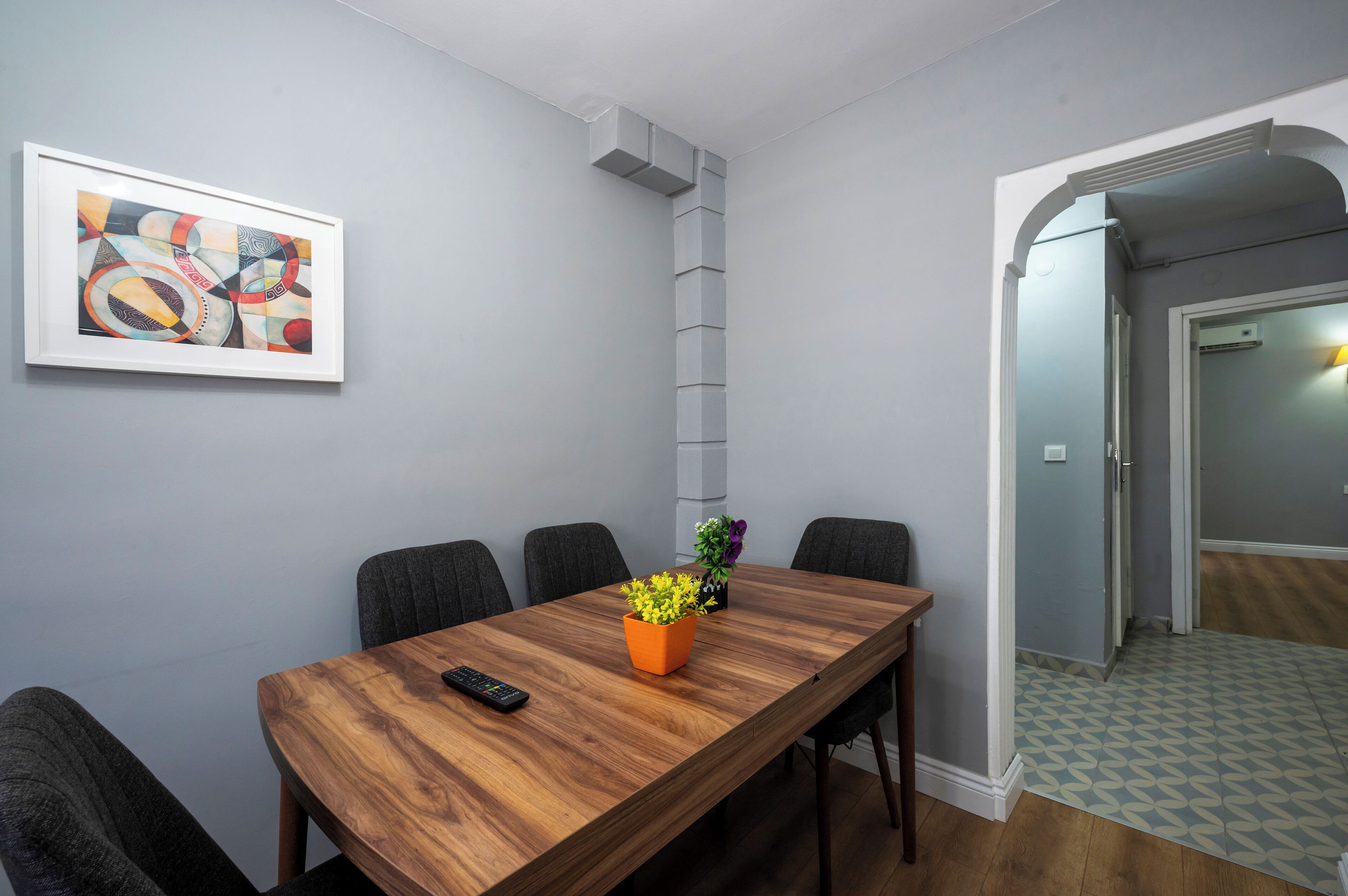 A conference room with a wooden table, chairs, a framed abstract painting, and two potted plants.