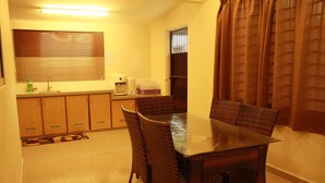 A dining area with a table and chairs, a kitchen with cabinets and appliances, and a window with blinds.