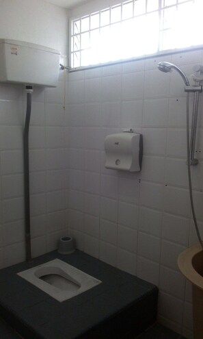 A small, basic bathroom with a toilet, a paper towel dispenser, and a shower.