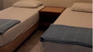 A small, simple room with two single beds, each with a pillow and a blanket. There is a nightstand between the beds and a small table with a lamp. - 37 First Island (George Town)