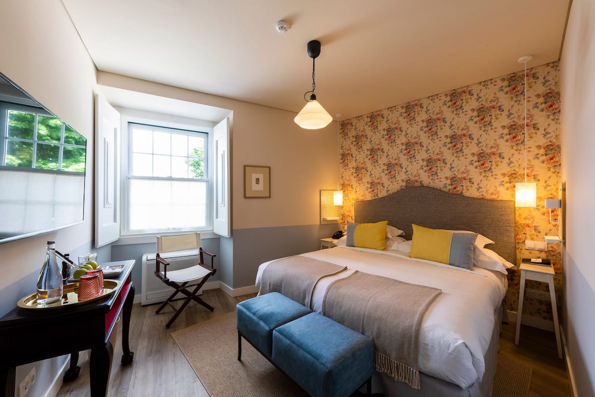 A bedroom with a large bed, bedside lamps, a desk with a chair, and a window with a view of trees.