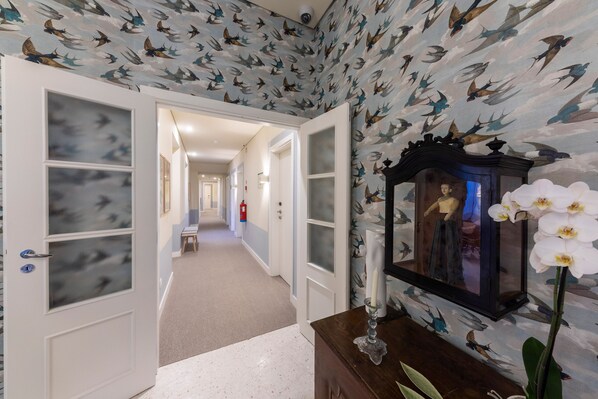 A hallway with patterned wallpaper, a framed portrait, and a white orchid.