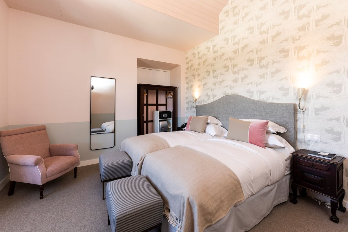 A bedroom with a large bed, a chair, a bench, a nightstand, a mirror, and a wardrobe.