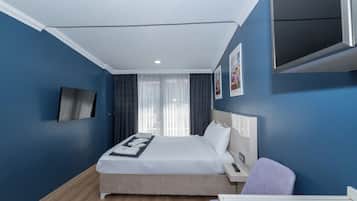 A modern hotel room with a large bed, a desk, a chair, a TV mounted on the wall, and a window with curtains.