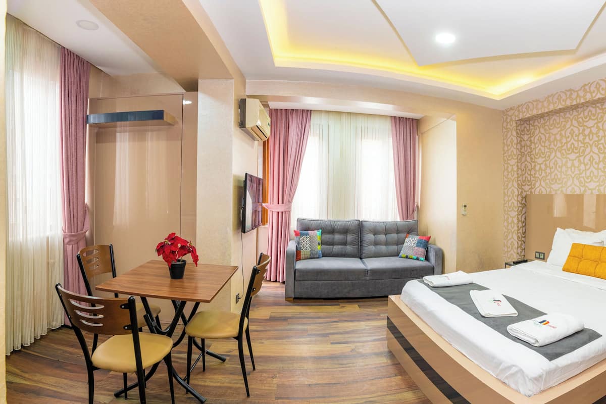 A hotel room with a bed, a sofa, a dining table with chairs, and a small table with a potted plant.