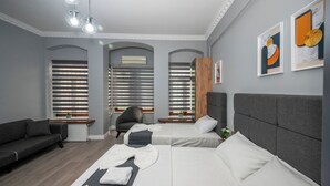 Una habitación de hotel moderna con un sofá gris, dos camas individuales, un cabecero gris y un techo gris.