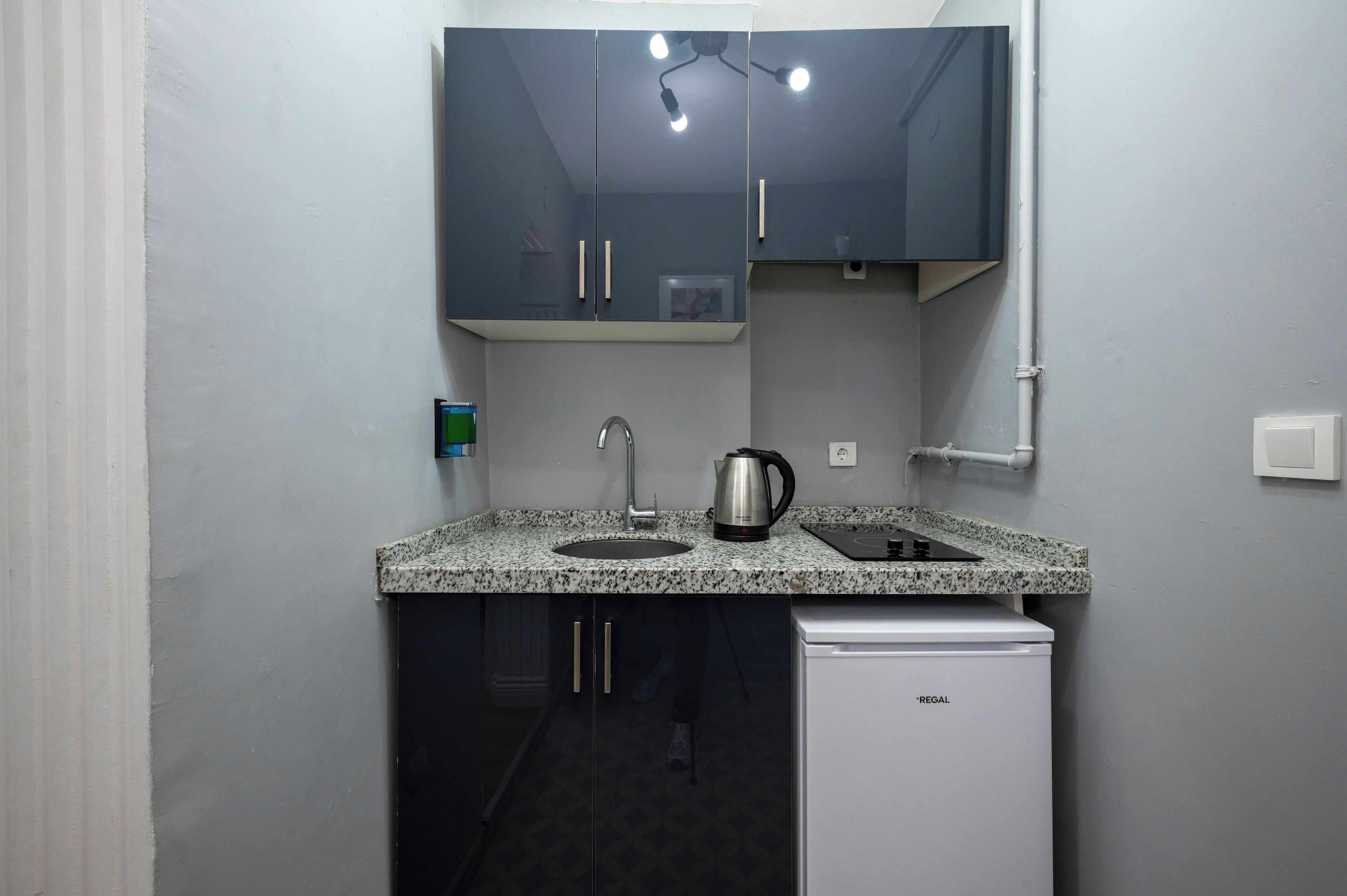 A compact kitchen with a granite countertop, a coffee maker, a sink, and a white refrigerator.