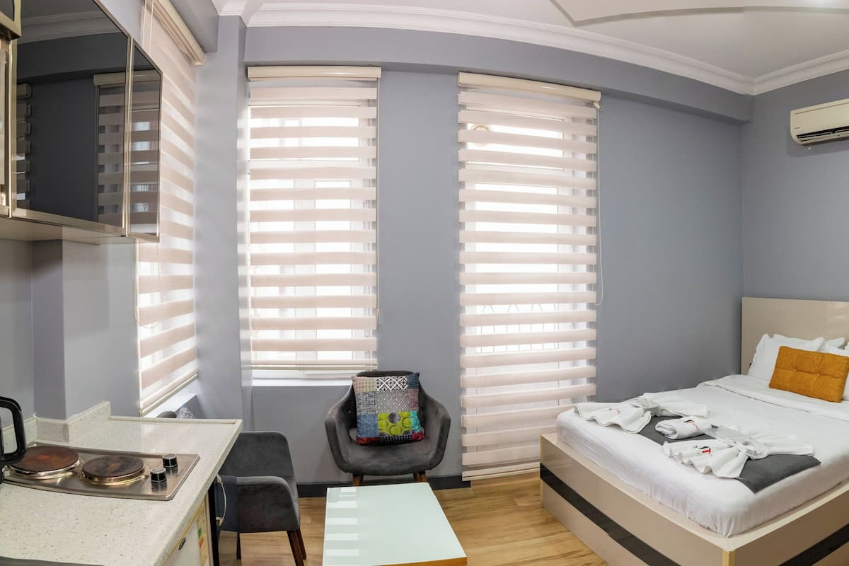 A hotel room with a bed, a desk, a chair, a small table, and a potted plant.
