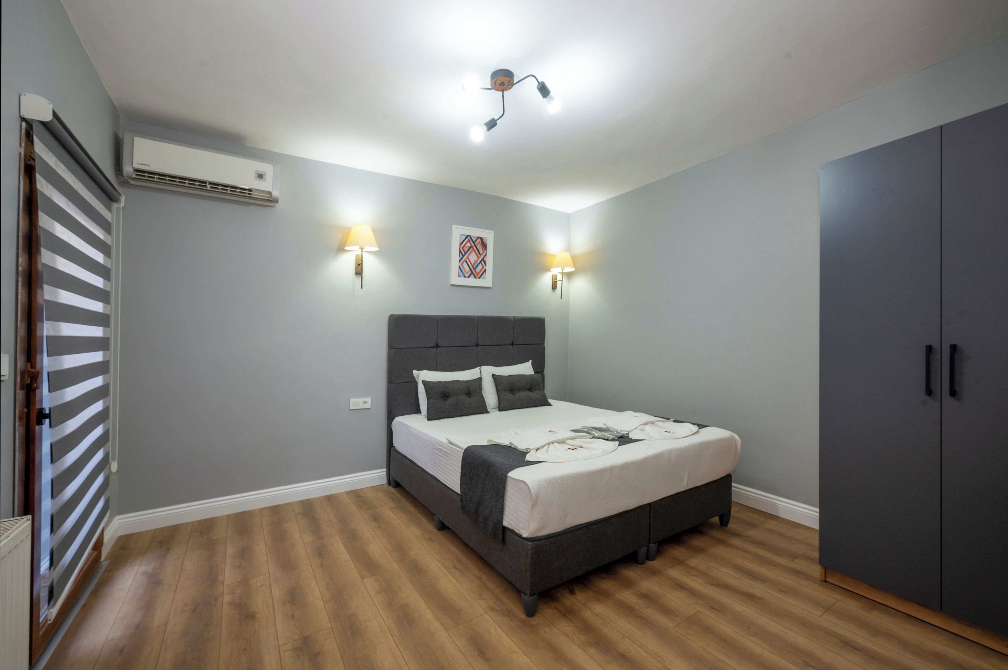 A bedroom with a bed, bedside lamps, an air conditioner, and a wardrobe.