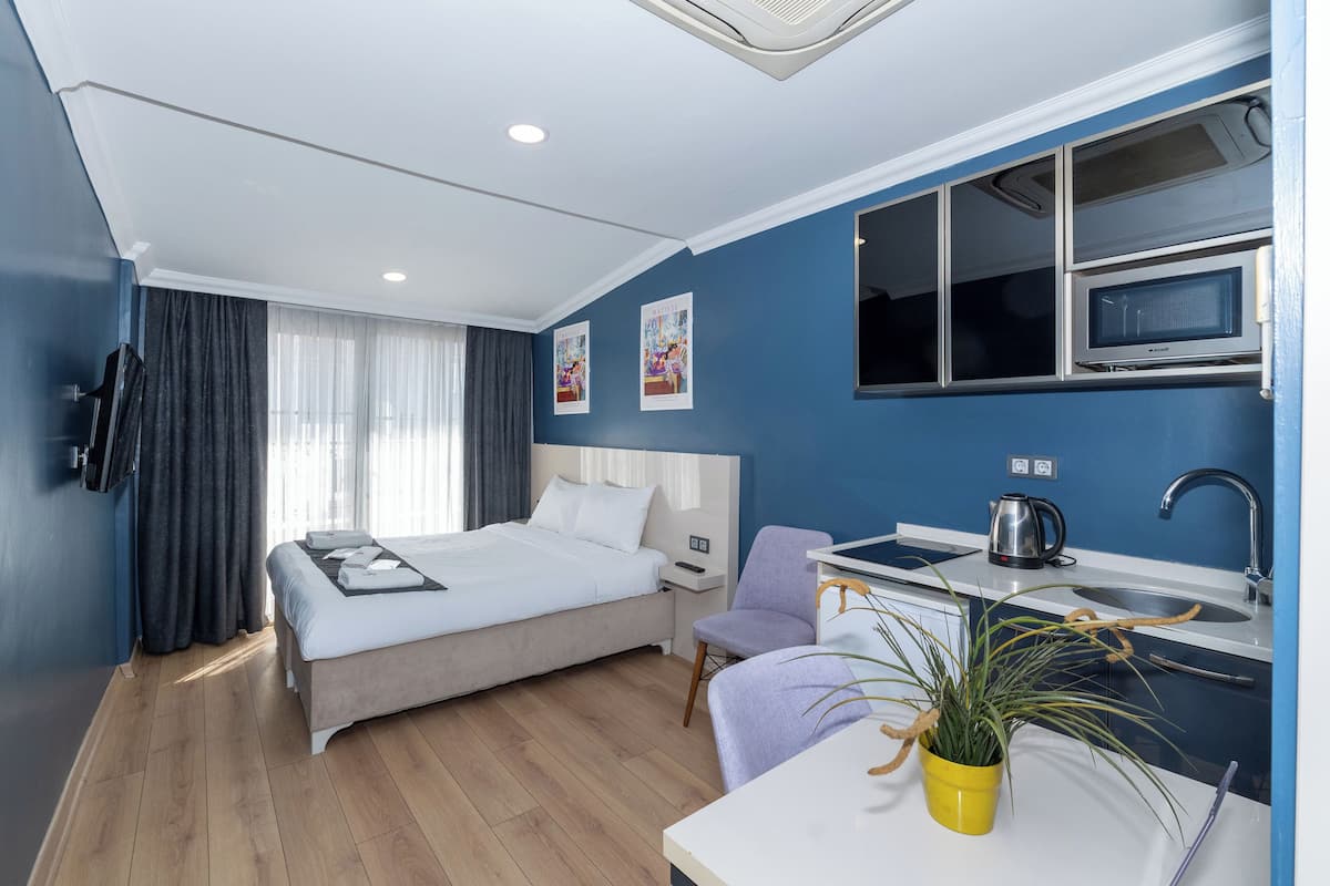 A modern hotel room with a bed, a desk with a microwave, a sink, and a potted plant.