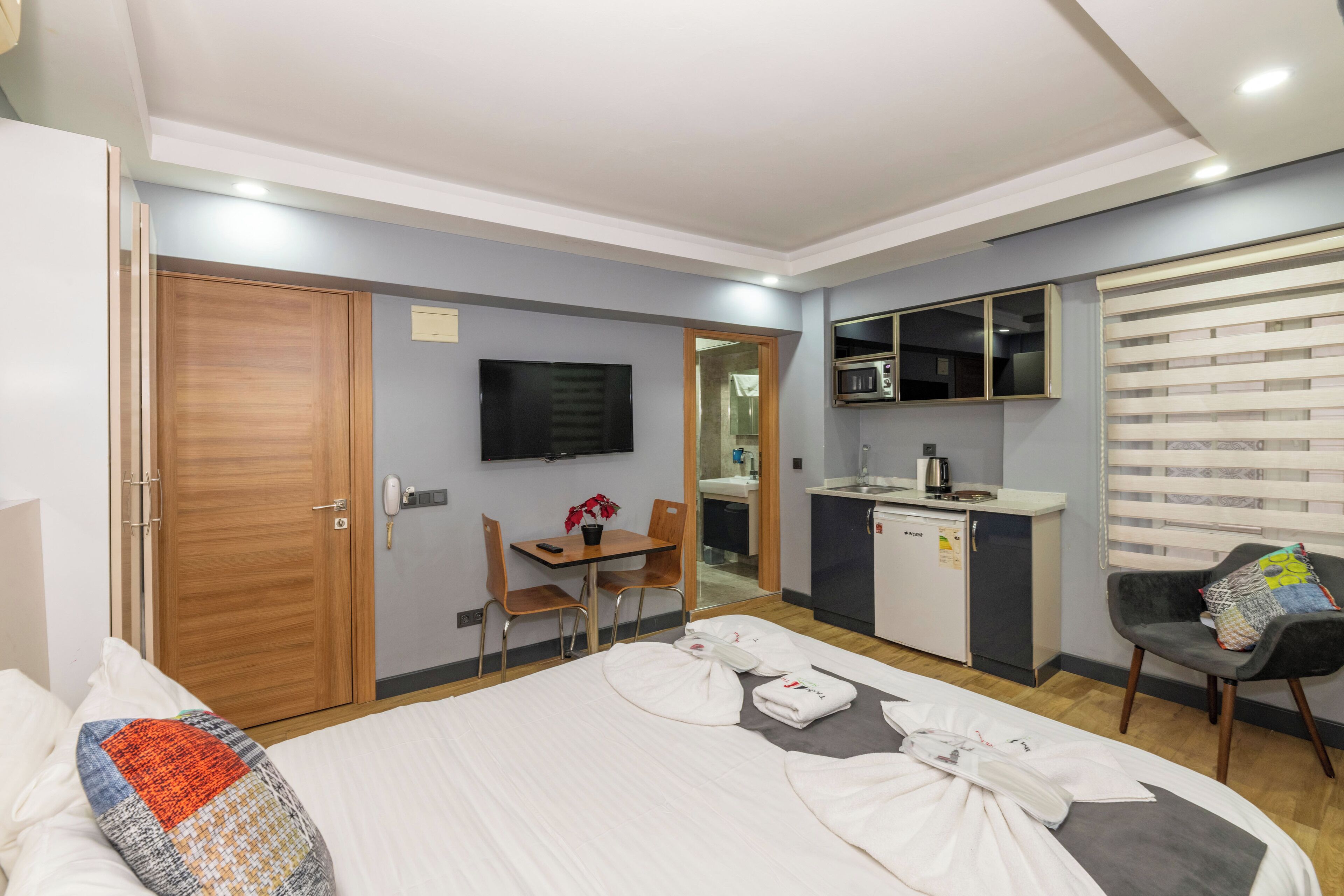 Habitación de hotel con cama, escritorio, silla, televisor, microondas y una pequeña kitchenette.