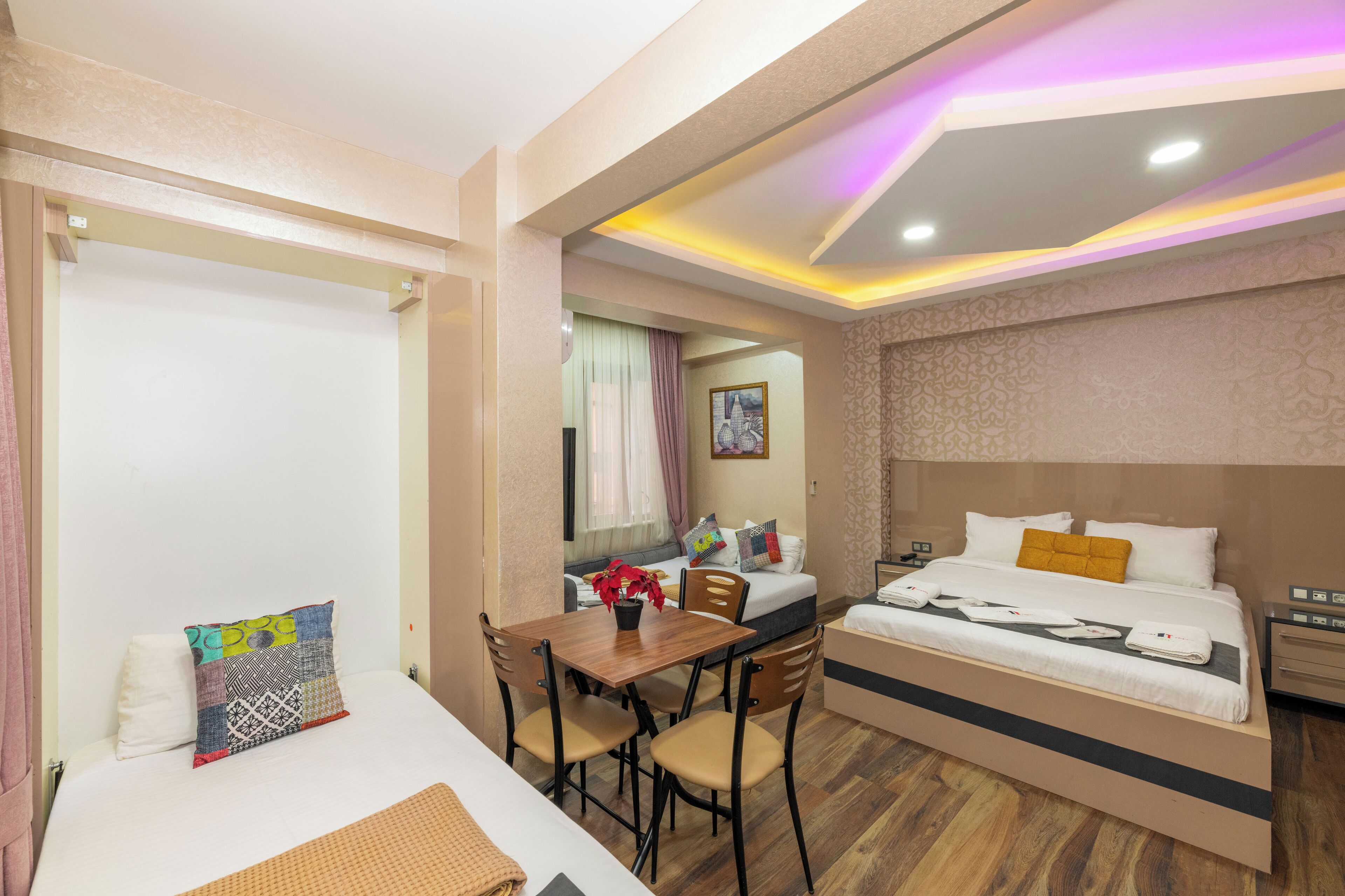 A hotel room with a bed, a desk, and a chair. There is a window with curtains, a wall clock, and a painting on the wall.