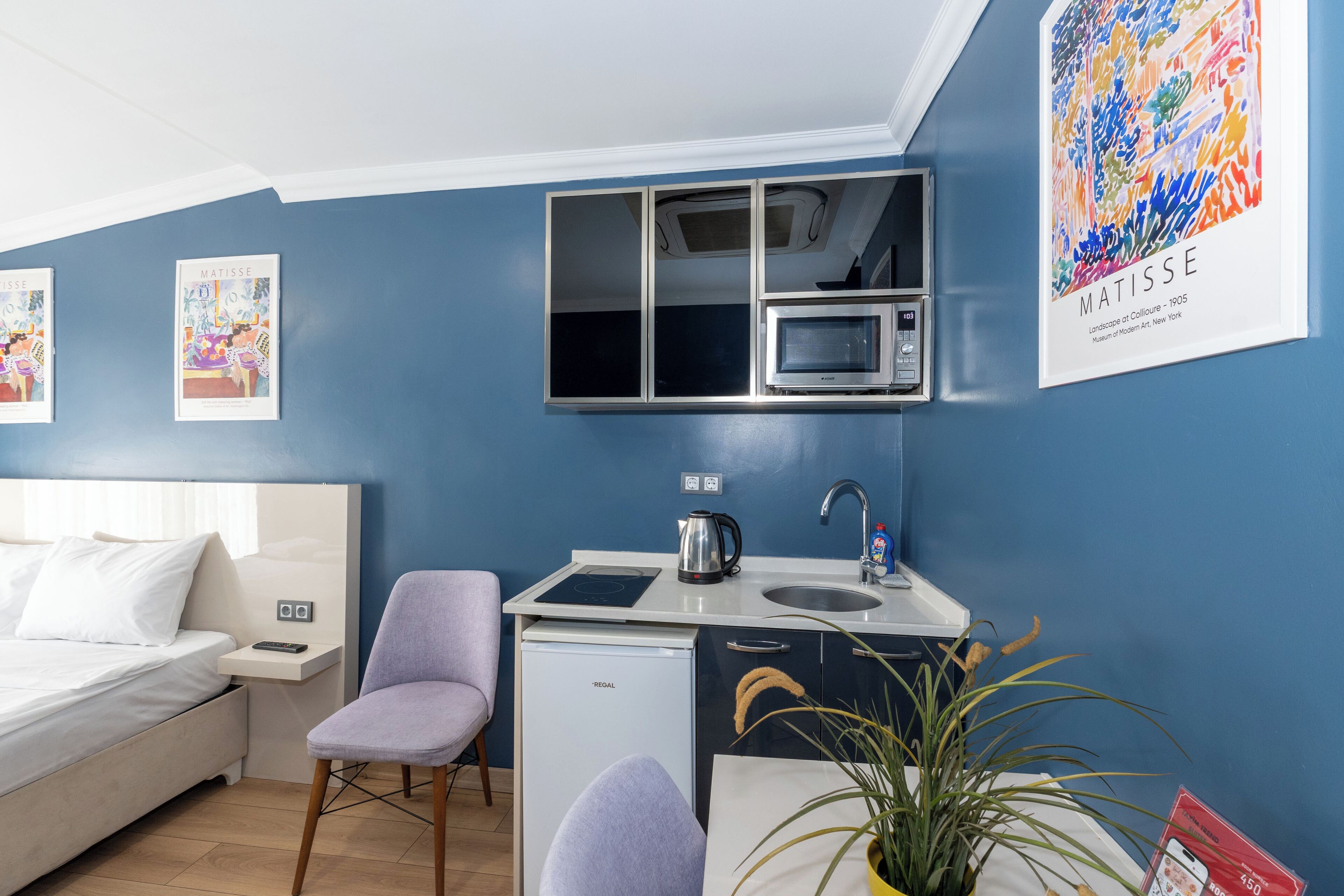 A compact hotel room with a bed, a small kitchenette, a microwave, and a chair.