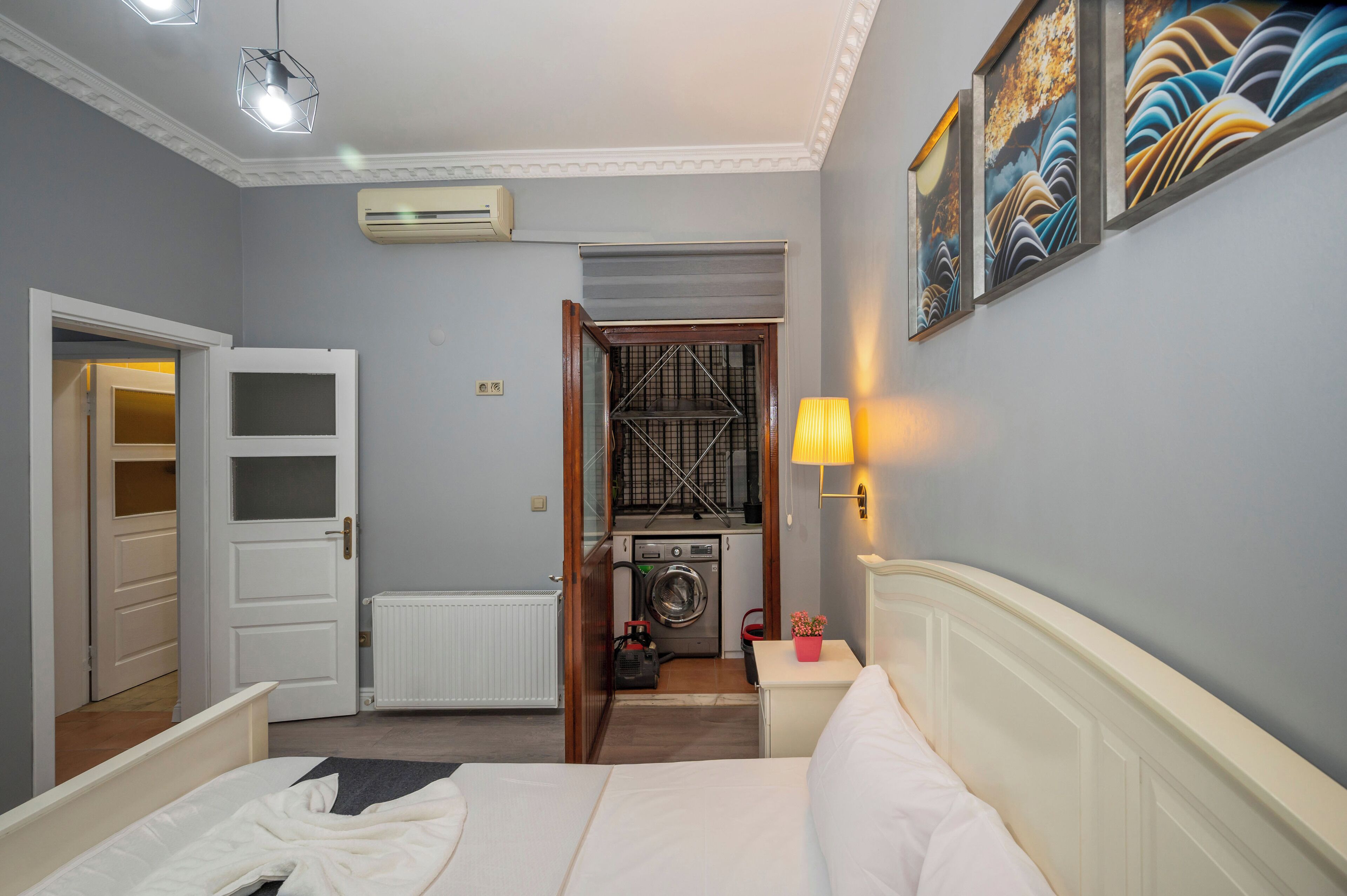 Habitación de hotel con cama, lavadora, radiador y puerta que da a otra estancia.